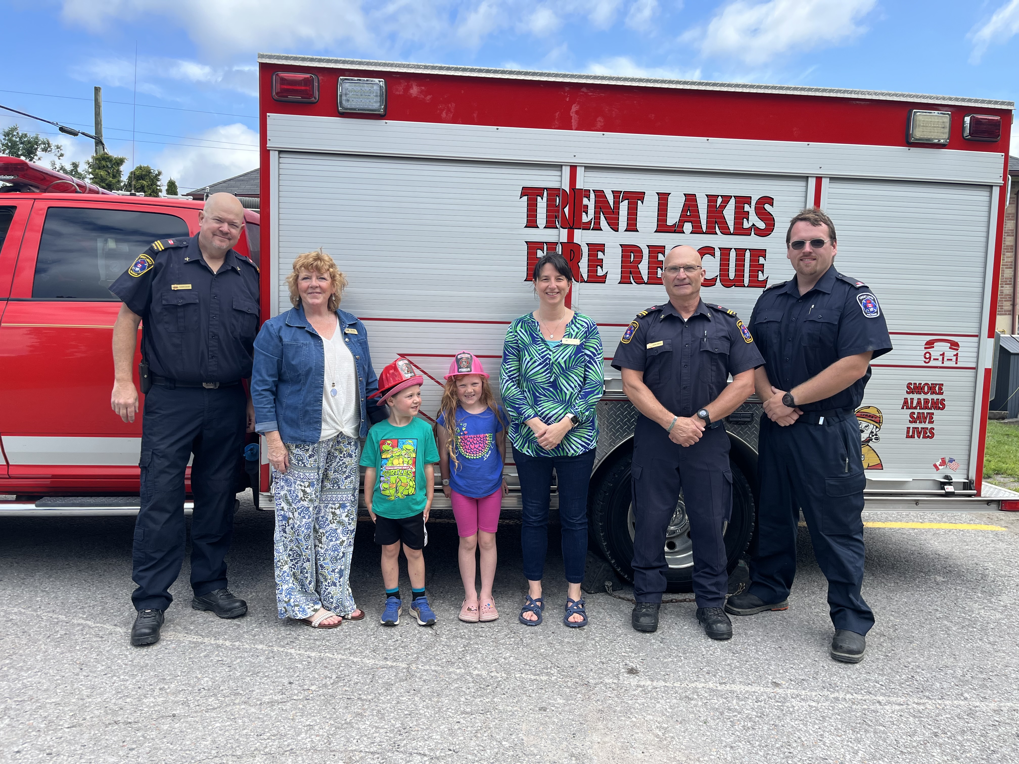 Children and firefighters stand in front of fire truck.